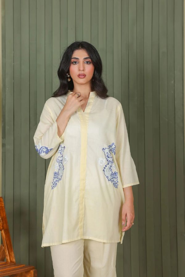 Woman wearing a light-colored outfit with blue embroidery against a green background