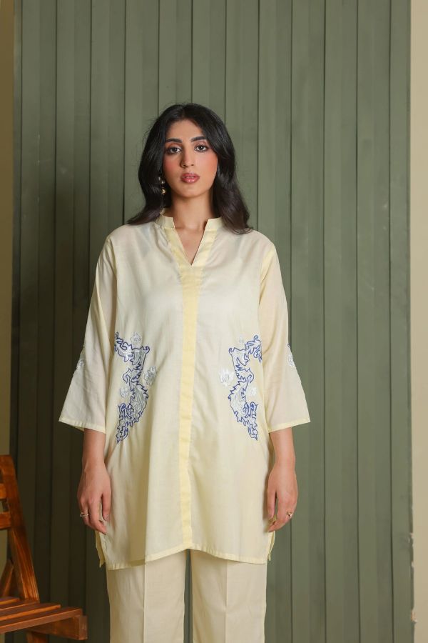 Woman wearing a light-colored outfit with embroidery against a green wall.