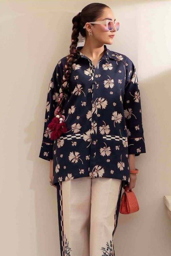Woman wearing a navy blue floral top and light-colored pants, holding a red bag indoors.