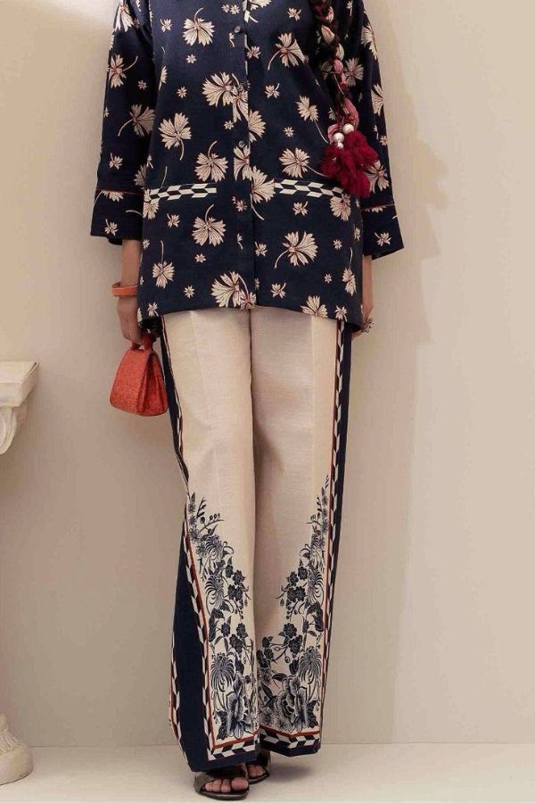 Person wearing a navy floral top and white pants with black floral patterns, holding a red clutch.