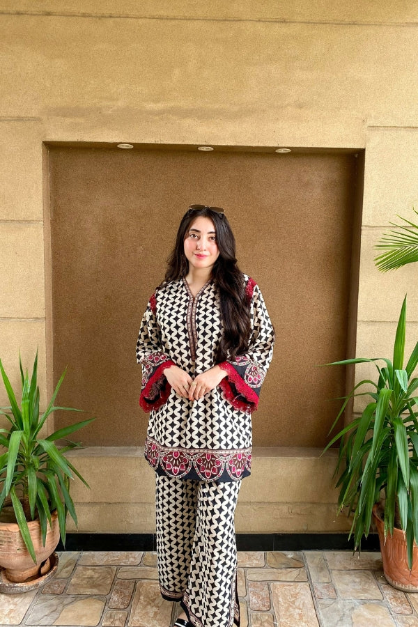 Woman in a patterned outfit standing in front of a beige wall with plants on either side.
