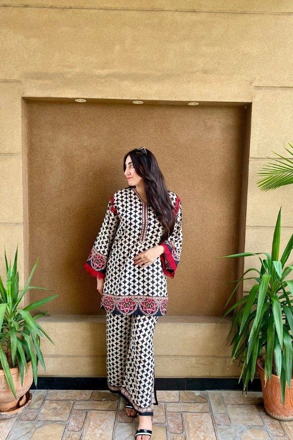 Woman in a patterned outfit standing against a beige wall with plants around.
