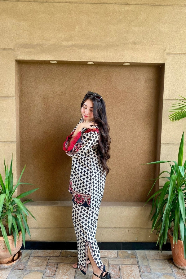 Woman in a black and white checkered dress standing in front of a beige wall with plants on either side.