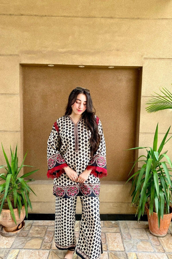 Woman in a patterned outfit standing in front of a beige wall with plants.