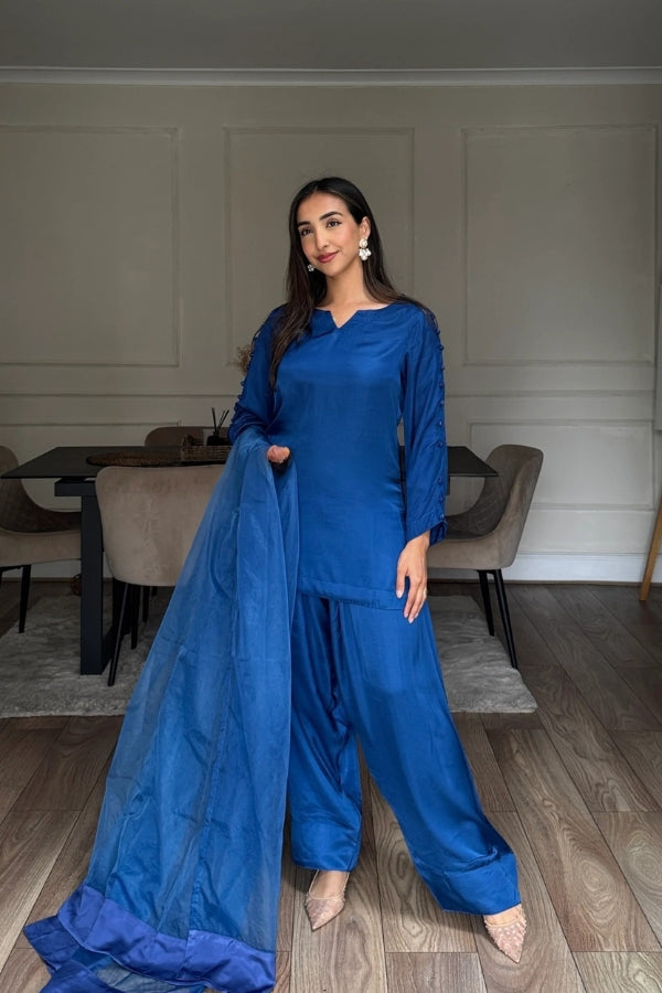 Woman in a blue outfit standing in a room with wooden flooring and neutral walls.