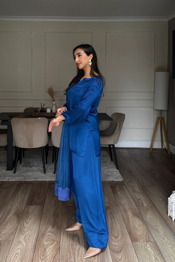 Woman in a blue outfit standing in a room with wooden flooring and neutral decor.