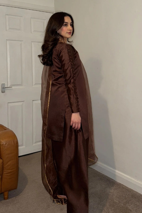 Woman wearing a brown outfit standing in a room with a white door and beige carpet.