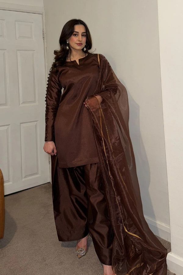 Woman wearing a brown traditional outfit standing indoors.