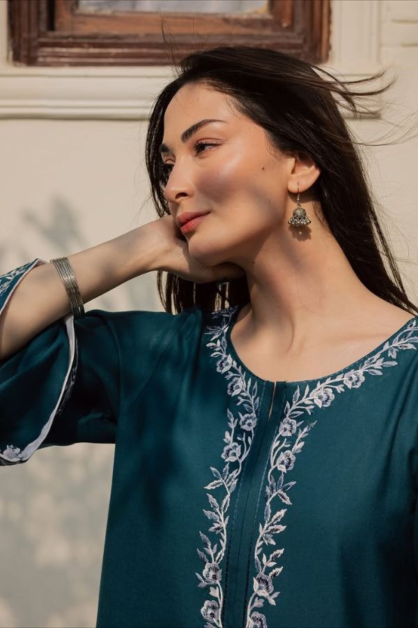 Woman wearing a teal embroidered top with a neutral background