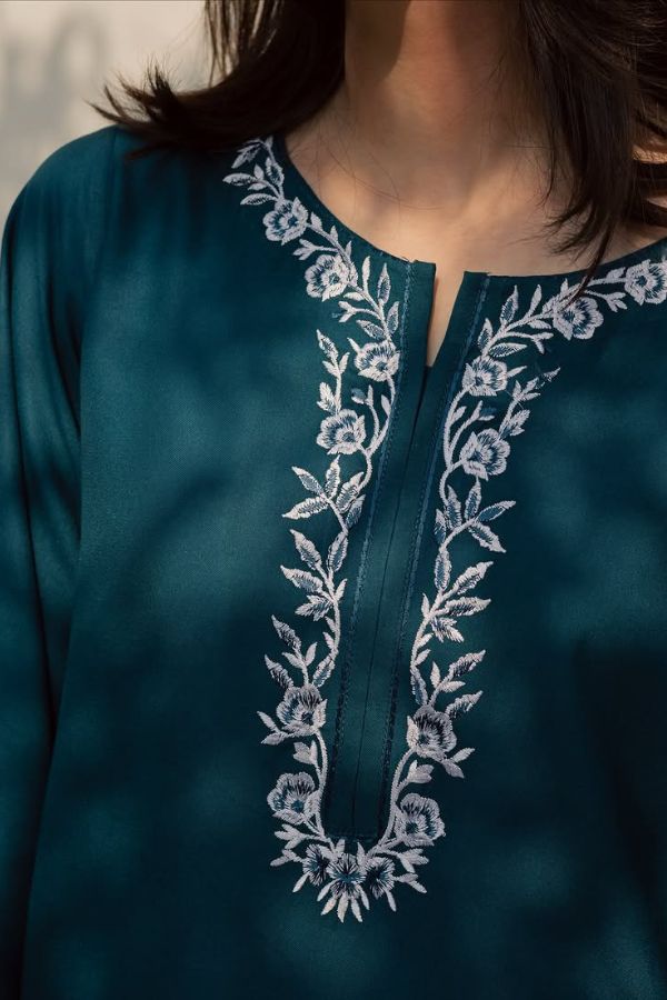 Teal top with white floral embroidery on a blurred background
