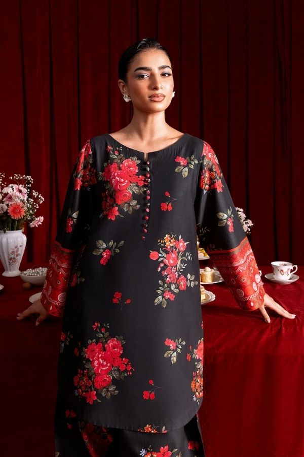 Woman wearing a black floral dress with red flowers against a red curtain background