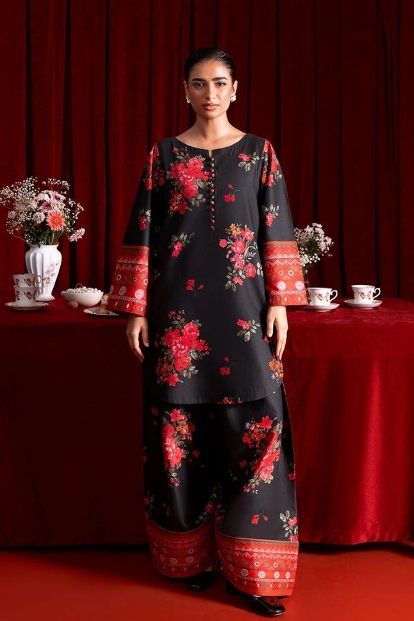 Woman wearing a black floral outfit standing in front of a red curtain with decorative elements.