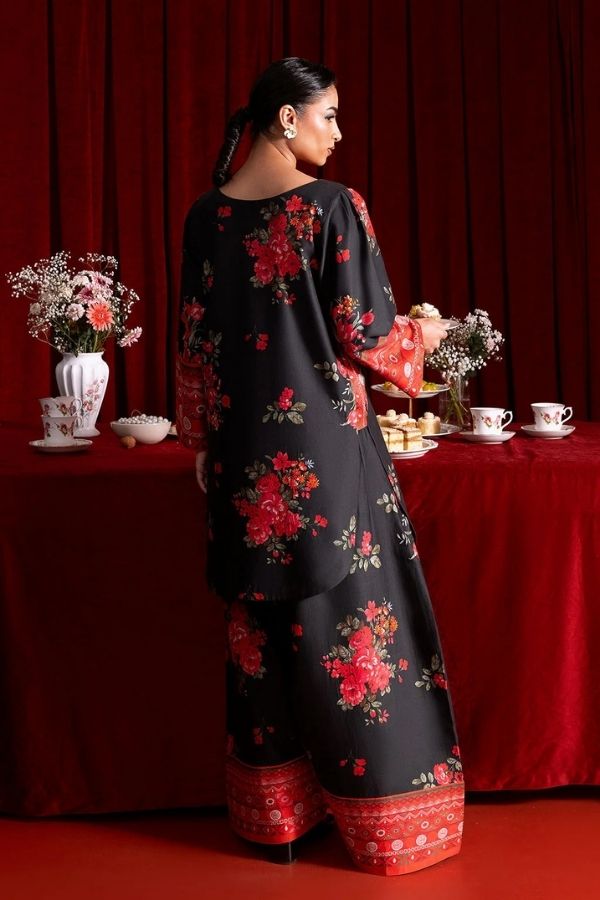 Woman in a black floral dress standing in front of a red curtain with a table setup.