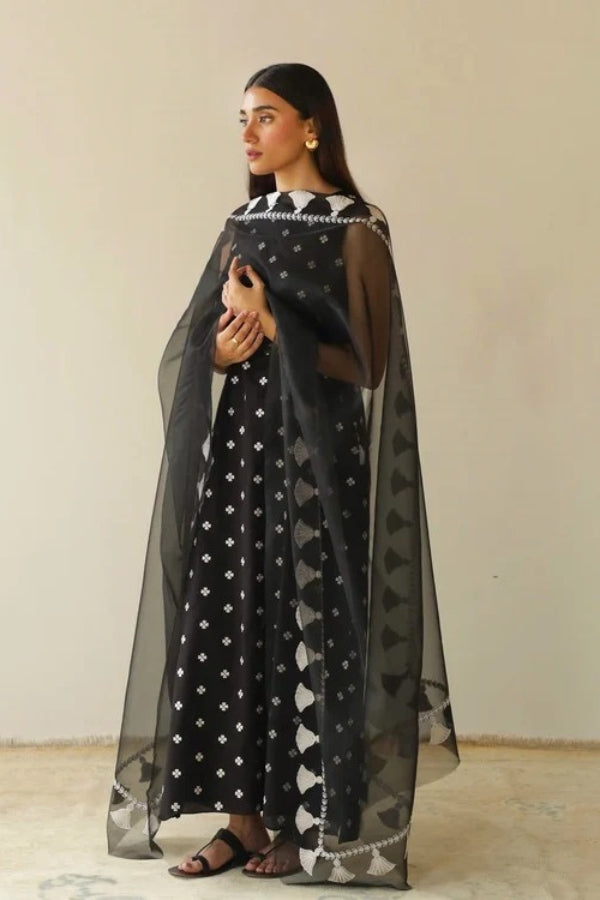 Woman wearing a black and white patterned outfit with a sheer black dupatta against a beige background
