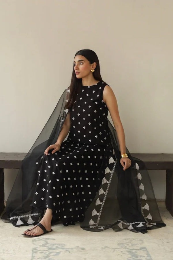 Woman in a black and white patterned dress sitting on a bench with a plain background