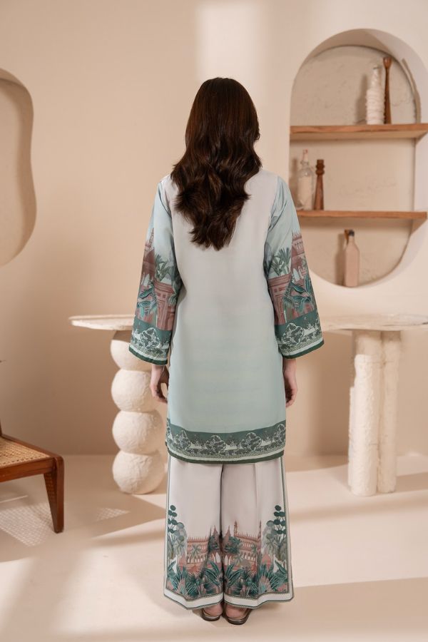 Woman wearing a light blue and white traditional outfit with floral patterns in a minimalistic room.