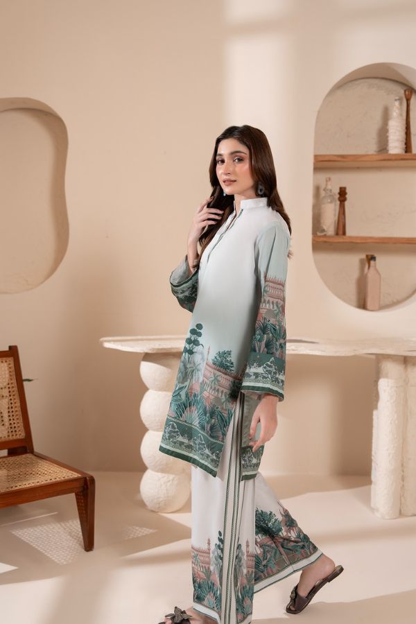Woman in a light blue and white outfit with green patterns in a modern interior setting.