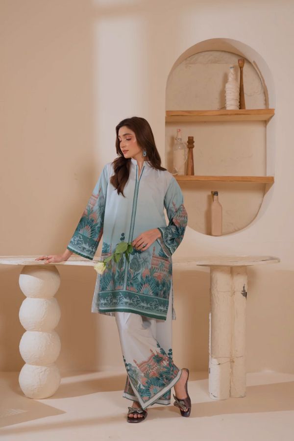 Woman in a light blue embroidered kurta with white pants standing in a minimalistic room.
