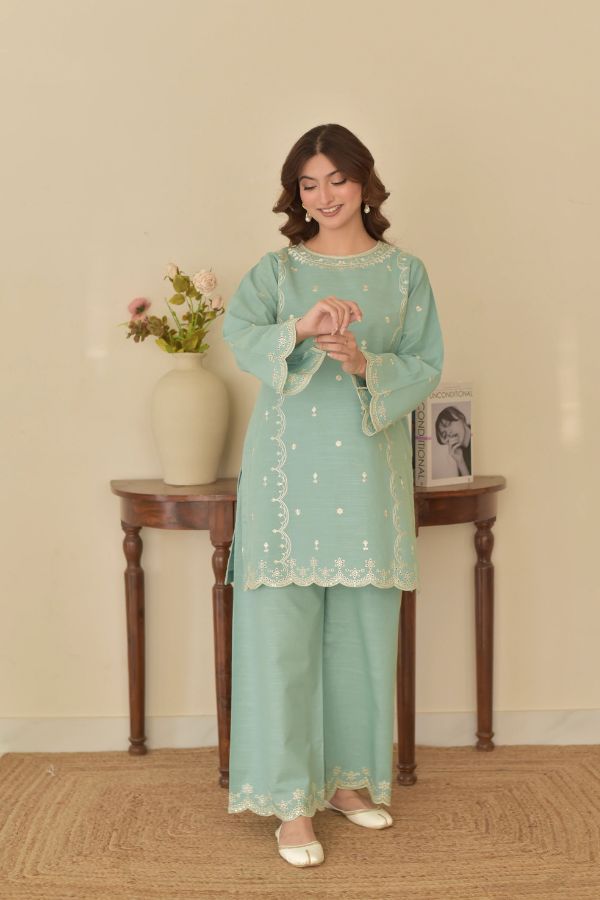 Woman in a light blue traditional outfit standing in a room with a table and vase.
