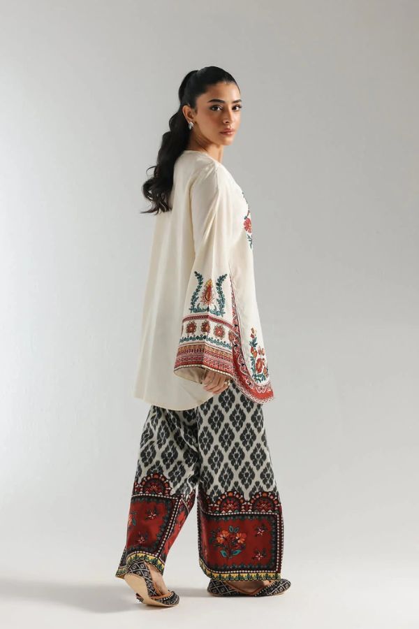Woman wearing a traditional outfit with embroidered top and patterned pants on a plain background