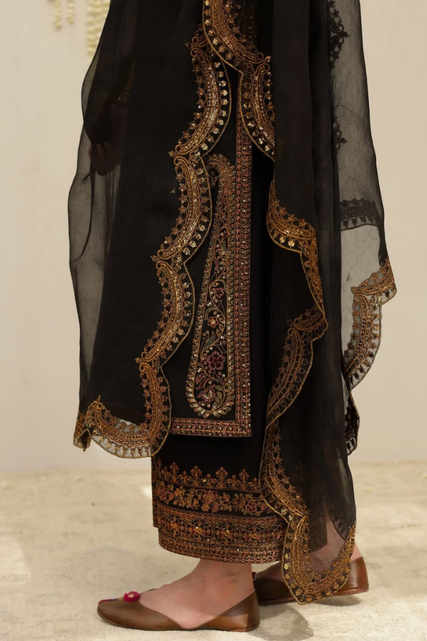 Black embroidered garment with gold detailing on a neutral background