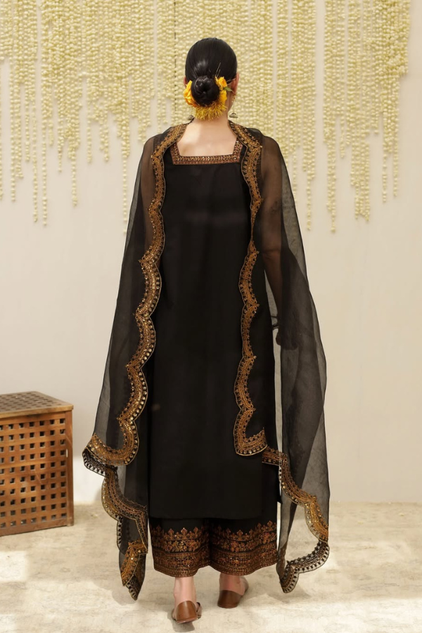 Person wearing a black traditional outfit with gold embroidery, standing against a neutral background.