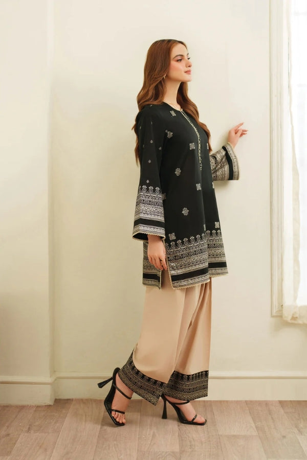 Woman wearing a black and white patterned outfit with beige pants in a room.
