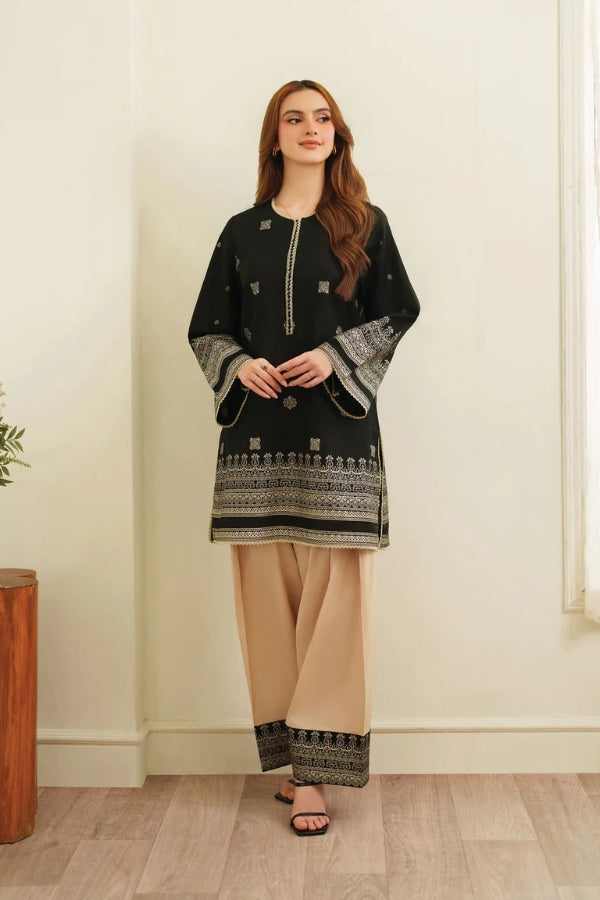 Woman wearing a black and beige traditional outfit with intricate patterns indoors.