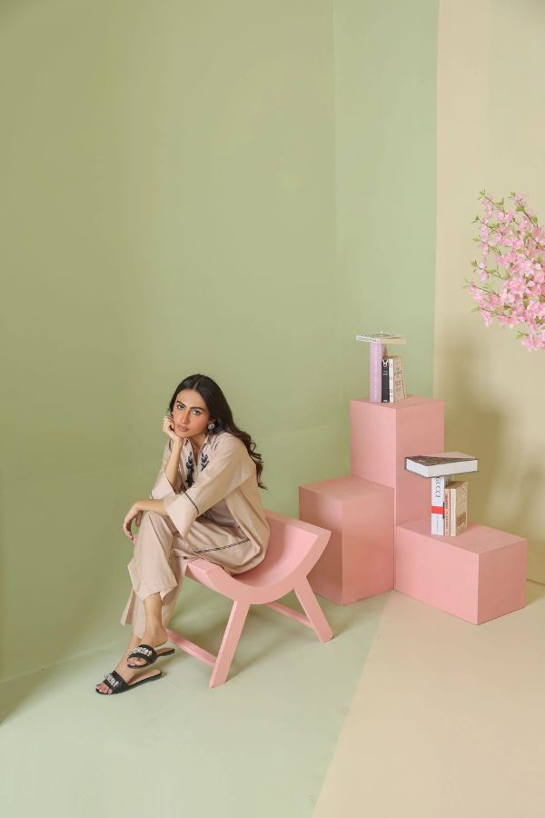 Woman sitting on a pink chair against a light green wall with pink floral decorations.