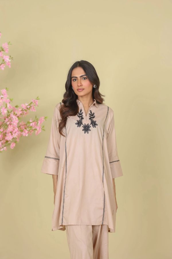 Woman wearing a beige outfit with black embroidery on a light green background