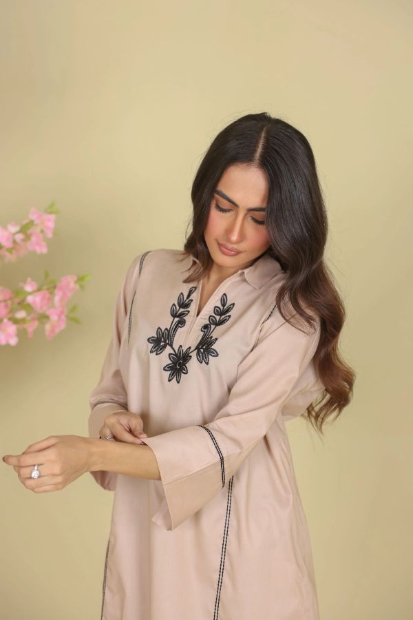 Woman wearing a beige outfit with black floral embroidery on a beige background