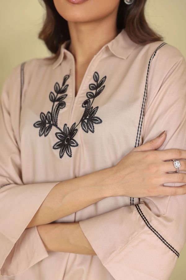 Beige shirt with black floral embroidery worn by a person, with a focus on the neckline.