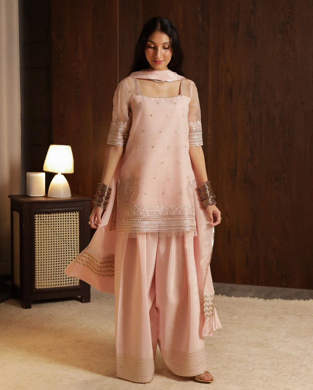 Woman wearing a pink traditional outfit with embroidery in a room setting.