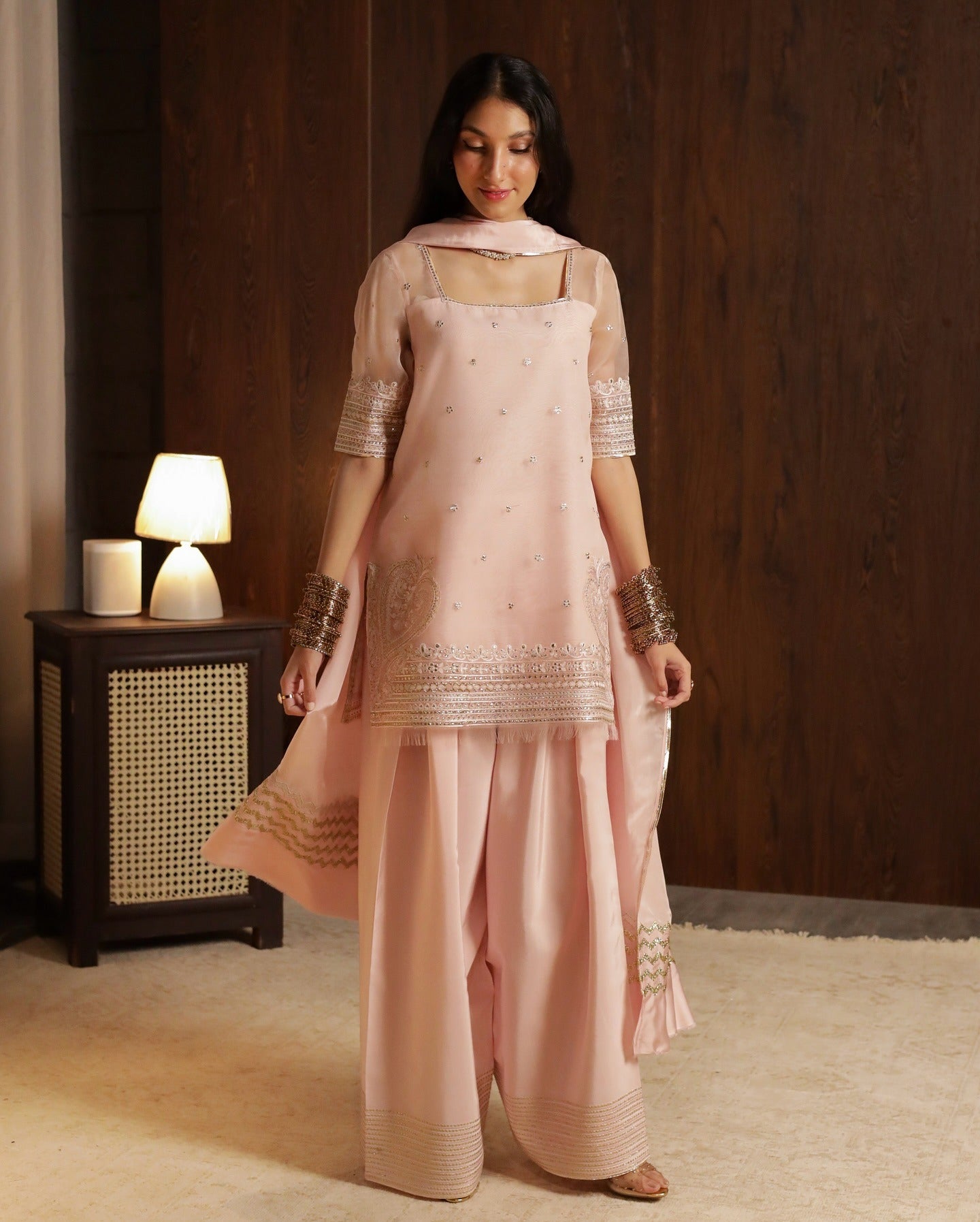 Woman wearing a pink traditional outfit with embroidery in a room setting.