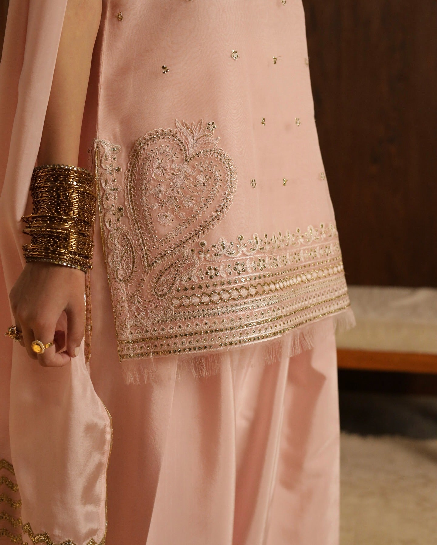 Pink embroidered outfit with gold details and a hand wearing gold bangles.