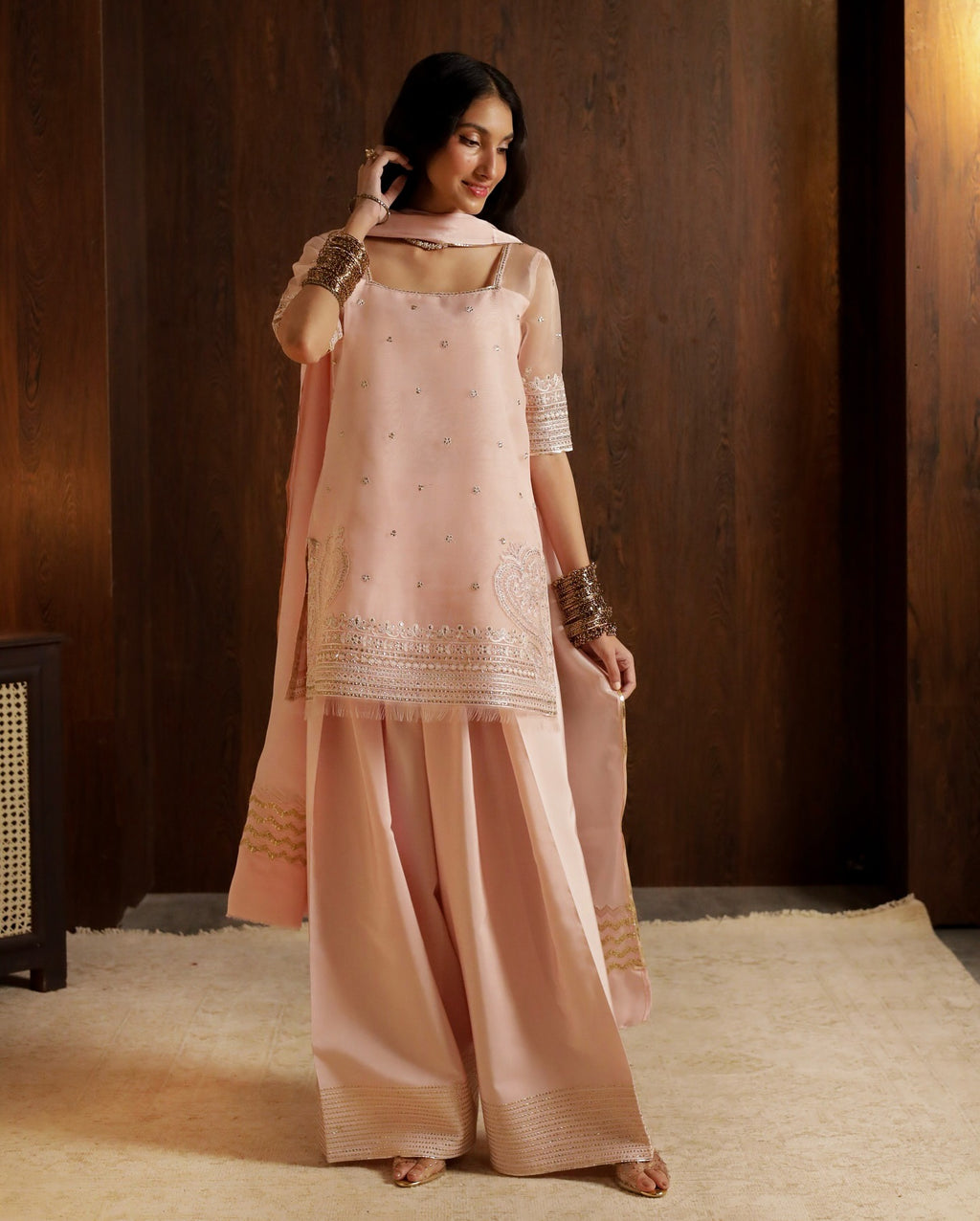 Woman wearing a traditional outfit with a pink dupatta and white top against a brown background